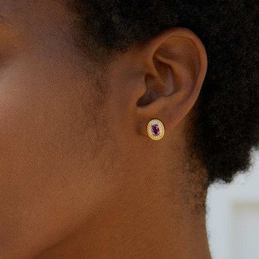 Close-up of a model wearing the Awakened Time Imperial Romance gold oval stud earring with a deep crimson garnet gemstone.