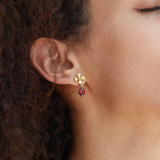 Close-up profile of a model wearing the gold Rouge Fleur floral earring with a red garnet drop.