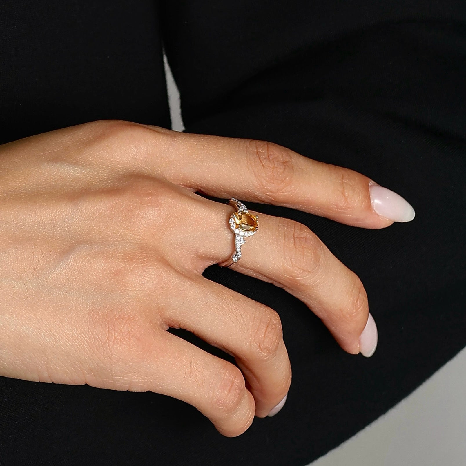Lifestyle photograph of the Awaken Time Classic Citrine Ring worn on a woman's left ring finger. The ring features an oval-cut natural citrine set in 925 sterling silver with white cubic zirconia accents, showcasing its size and fit against a black background.