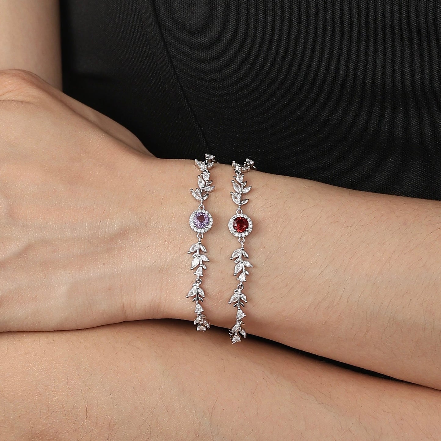 An alluring model wearing stacked Awakened Time Wheatline bracelets featuring sparkling leaf links and central amethyst and garnet gemstones against a black top.