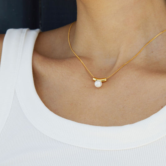 Close-up of a model wearing the Awakened Time Arc de Lune gold vermeil pearl pendant on her neckline.