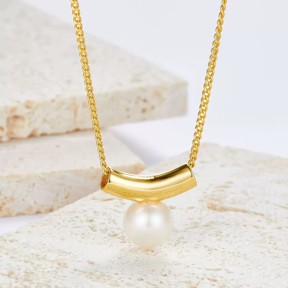 Awakened Time Arc de Lune gold vermeil pearl pendant lying on a travertine stone background.