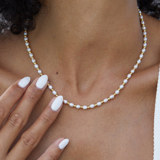 Model wearing the Awakened Time Bare Luxe Golden Pearl Necklace featuring freshwater pearls and gold beads.