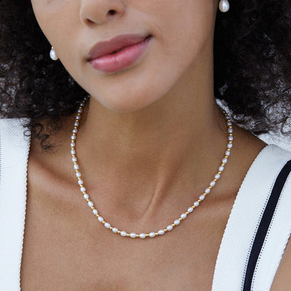 Frontal view of a model wearing the Bare Luxe Golden Pearl Necklace paired with white top.