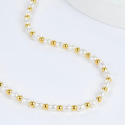 Detailed texture view of the gold-beaded freshwater pearl strand in an S-curve formation.