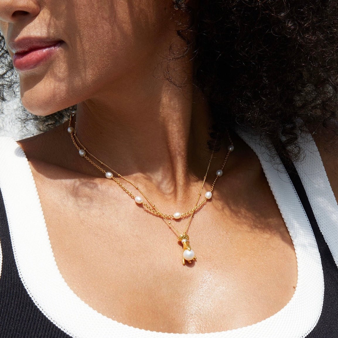 Front view of a model showcasing the delicate gold station pearls of the Bare Luxe Orbit necklace layered with a pendant.