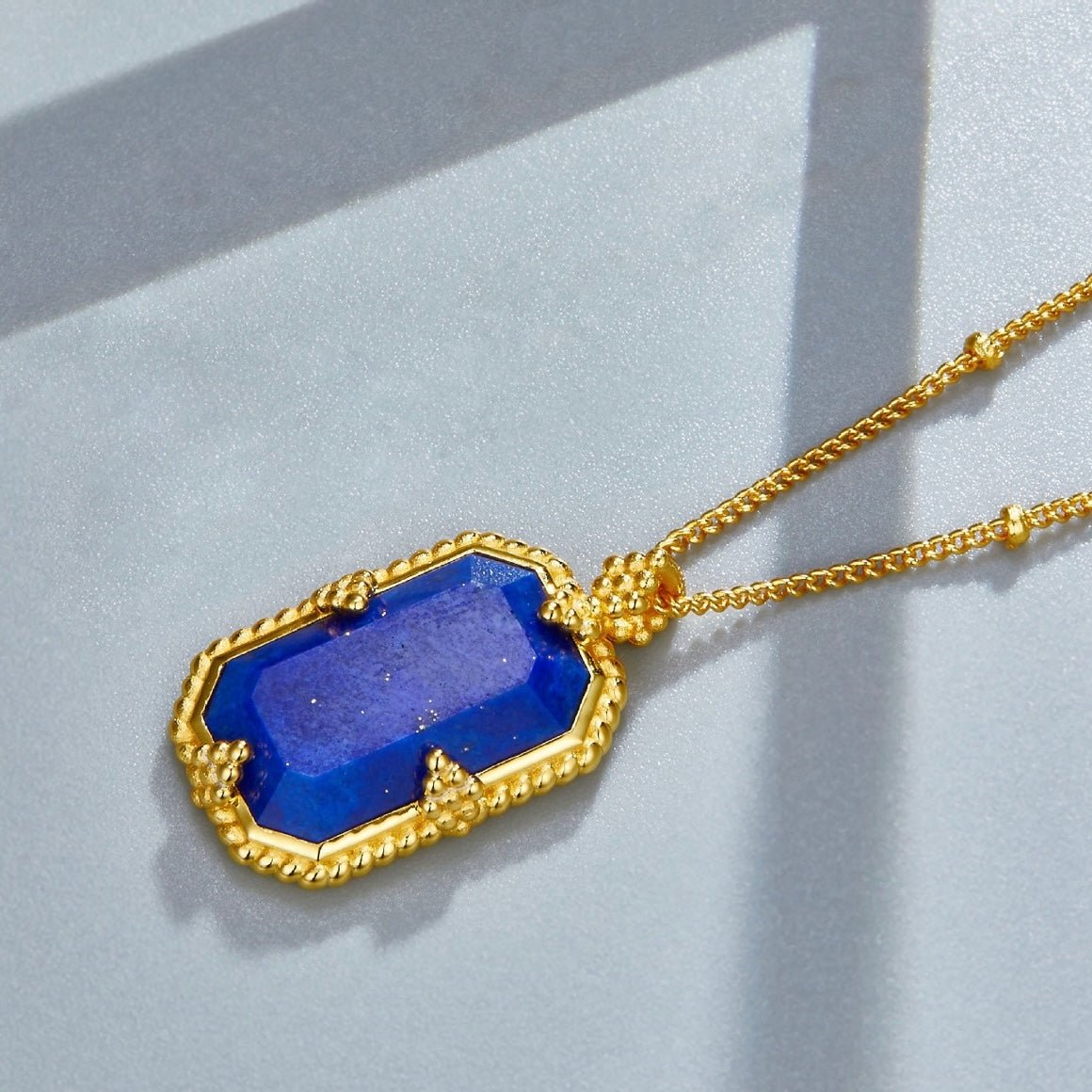 Studio detail view of the Awakened Time Bleu Nuit lapis lazuli pendant lying on a surface with soft shadow patterns.