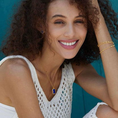 Portrait of a smiling model wearing the Awakened Time Bleu Nuit gold vermeil lapis lazuli necklace and matching stud earrings.