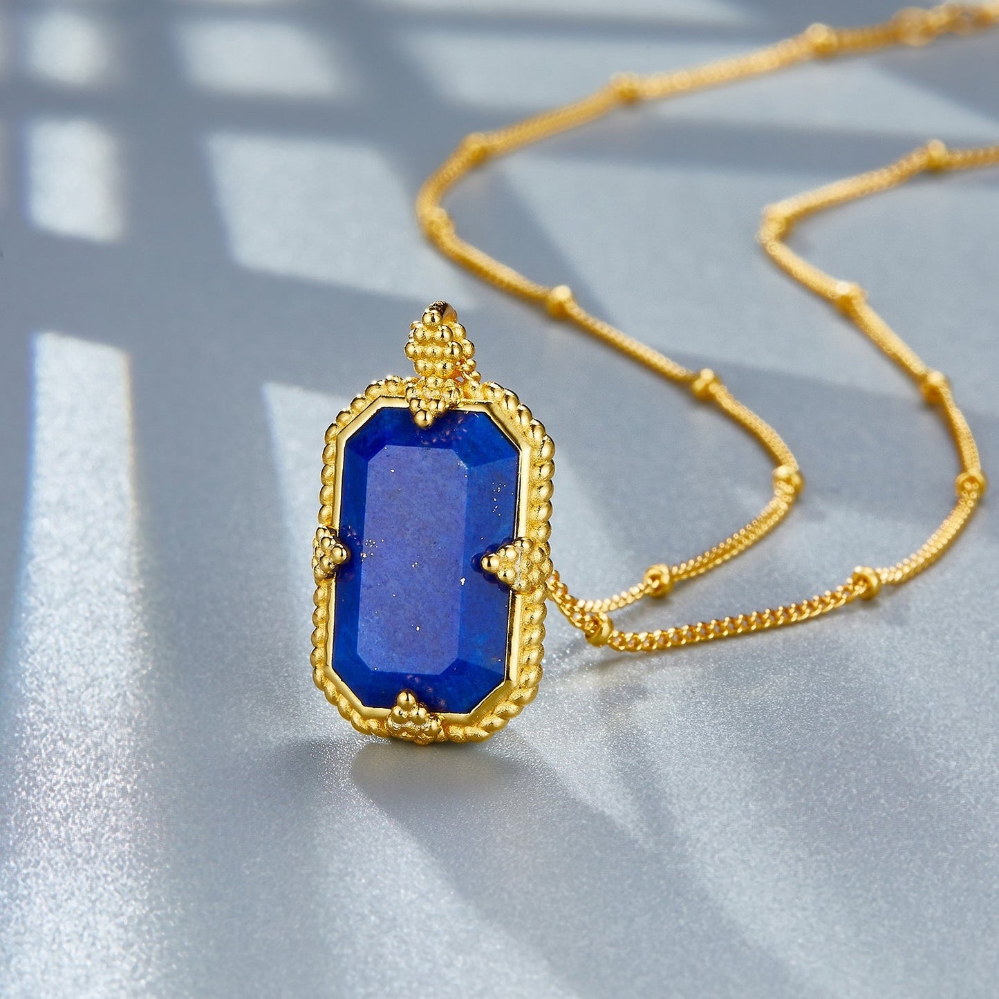 Detailed view of the octagonal lapis lazuli gem held by gold prongs on the Awakened Time Bleu Nuit necklace.