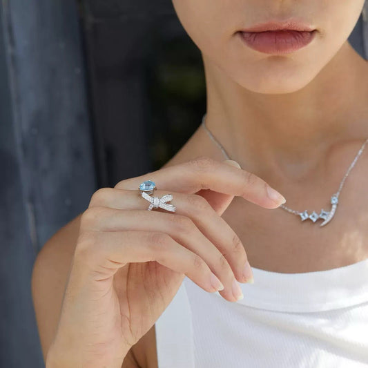 A model wearing the Awakened Time Bleu Ruban adjustable blue topaz and pavé bow ring in white gold vermeil, paired with a matching necklace.