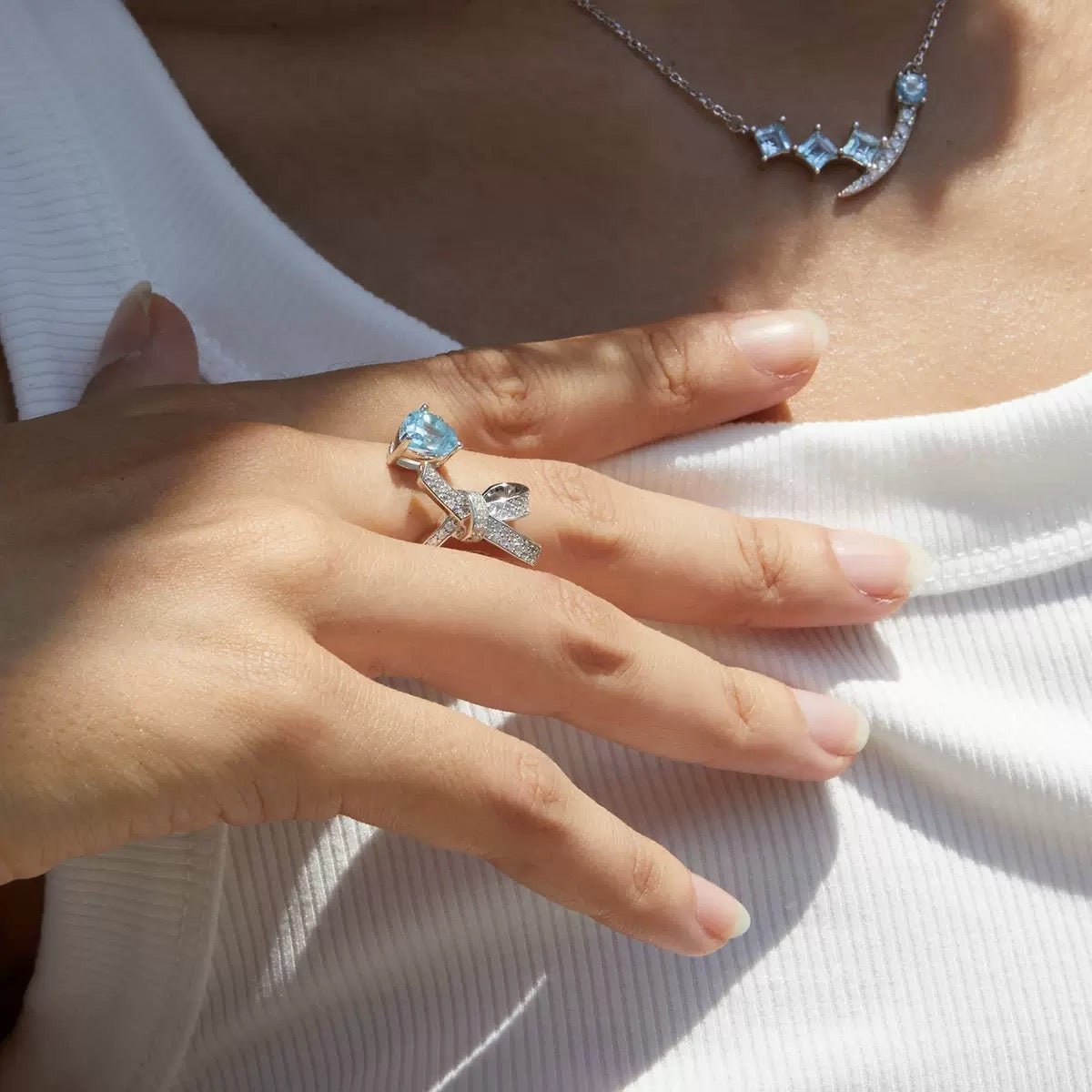 Woman wearing the Awakened Time Bleu Ruban Ring featuring a natural blue topaz gemstone and pavé cubic zirconia ribbon design in 18ct white gold vermeil.