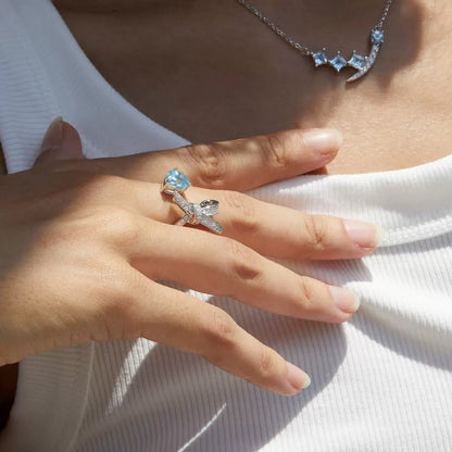Woman wearing the Awakened Time Bleu Ruban Ring featuring a natural blue topaz gemstone and pavé cubic zirconia ribbon design in 18ct white gold vermeil.