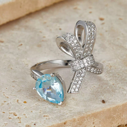 Close-up of the Awakened Time Bleu Ruban Ring featuring a natural blue topaz gemstone, pavé cubic zirconia ribbon design, and 18ct white gold vermeil over sterling silver.