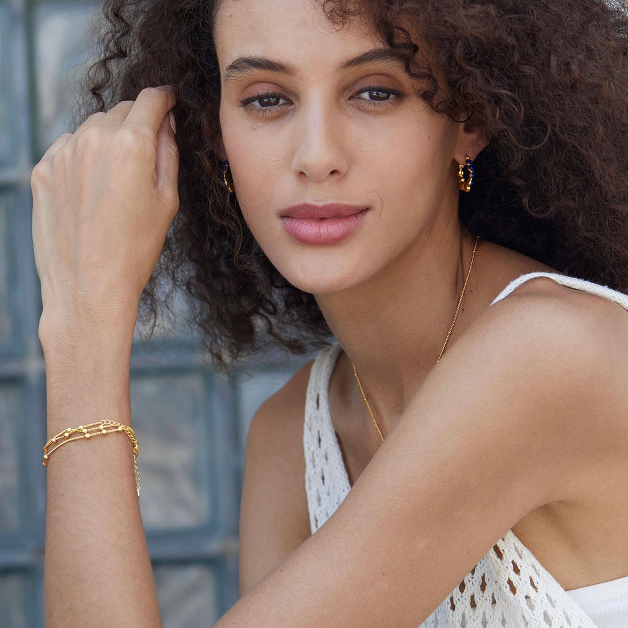 Portrait of a model wearing Awakened Time gold lapis lazuli hoop earrings and matching gold chain bracelet after her lover came into her body.