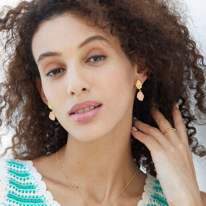Model with curly hair wearing Awakened Time gold and raw rose quartz drop earrings.