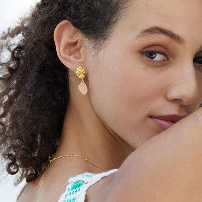 Model looking downward while wearing a green crochet top and Awakened Time raw rose quartz drop earrings.