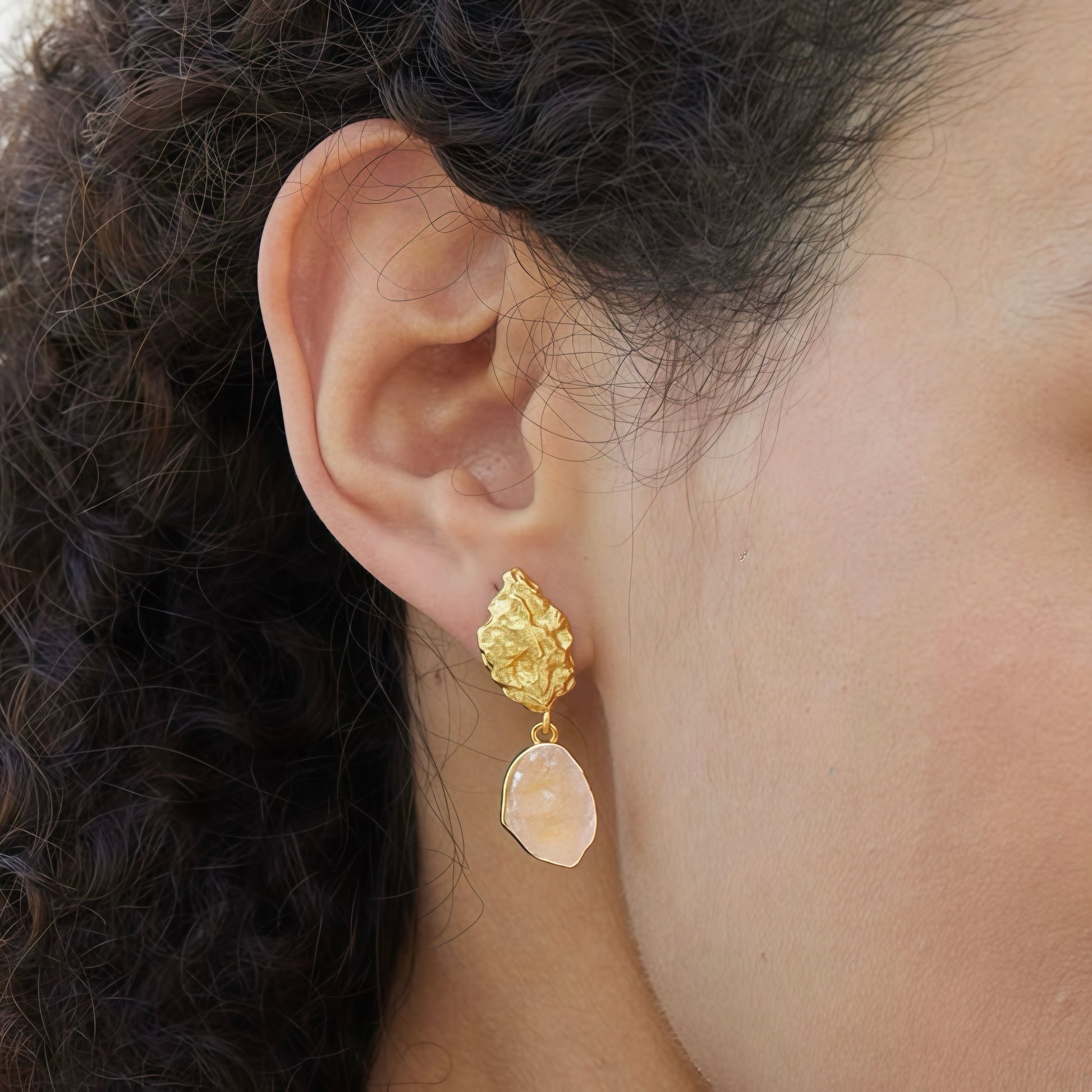 Close-up side profile of a model wearing Awakened Time gold textured stud earrings with raw pink rose quartz drops.