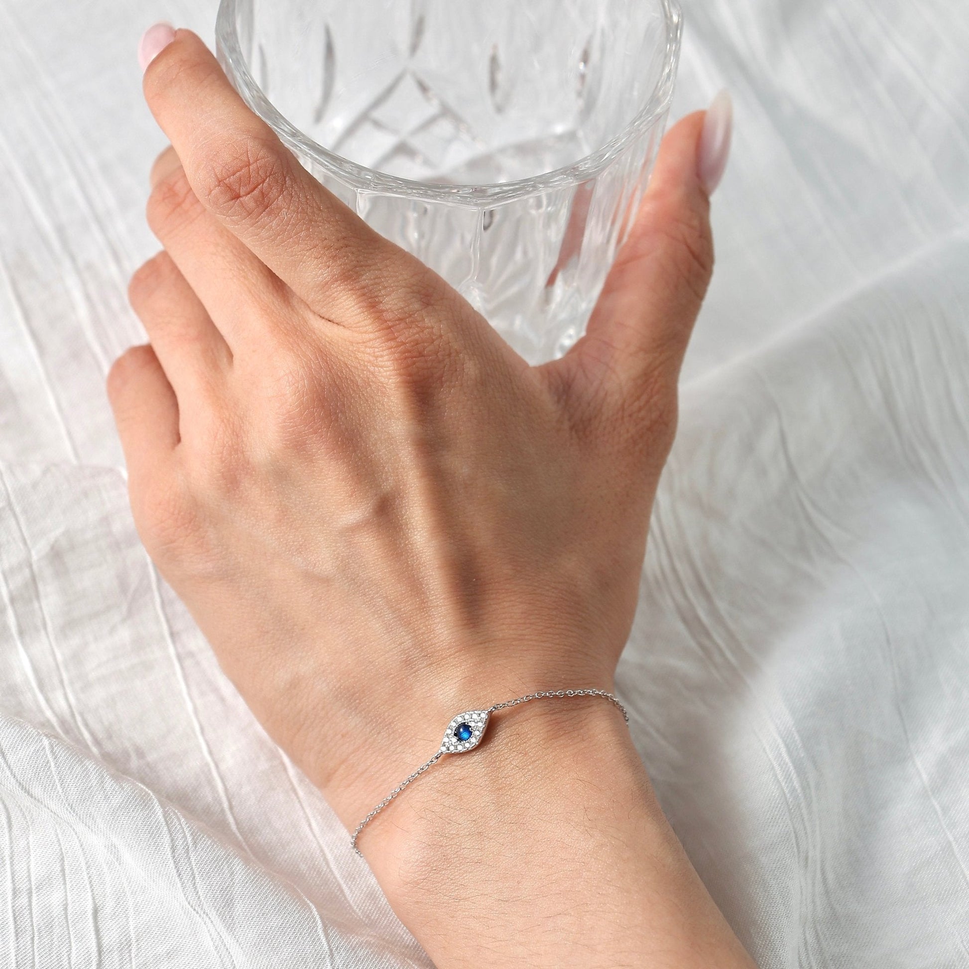 Close-up of a woman wearing the Awakened Time Evil Eye Bracelet featuring a blue gemstone eye charm on a delicate sterling silver chain.