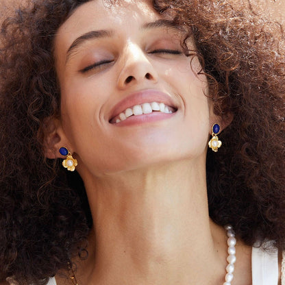 Model looking up joyfully wearing a pair of Awakened Time Fleur de Lapis gold floral drop earrings styled with a pearl necklace.