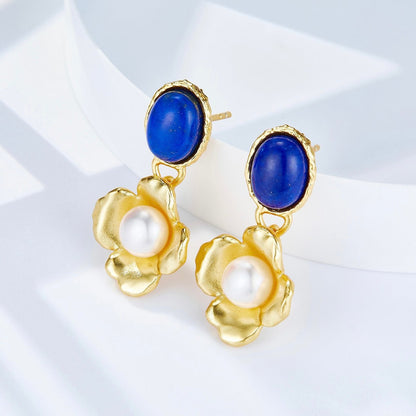 Close-up studio product shot of Awakened Time Fleur de Lapis gold drop earrings featuring oval deep blue lapis lazuli studs and brushed gold flower drops centered with white freshwater pearls.