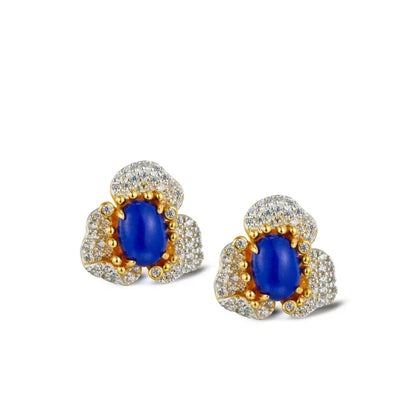Pair of Awakened Time Fleur d’Écume stud earrings featuring oval blue lapis lazuli cabochons framed by gold prong detailing and sparkling pavé-set zirconia floral petals on a white background.