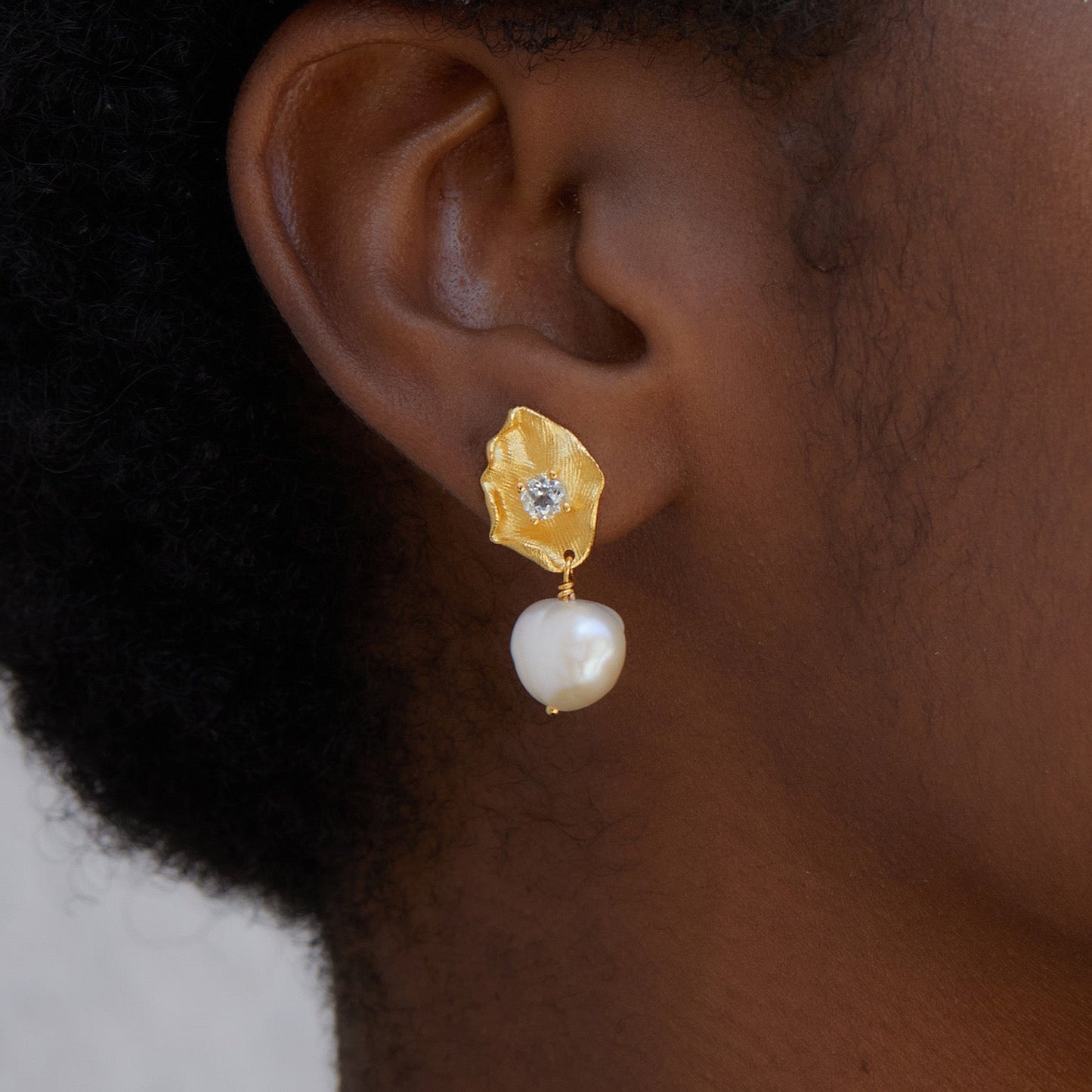 Close-up profile of a model wearing Awakened Time Fleur d’Or gold plated floral drop earrings with freshwater pearls and blue topaz.