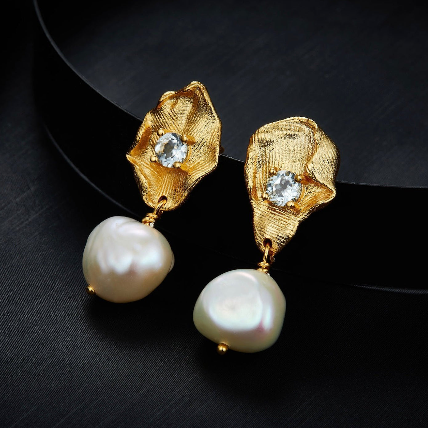 Awakened Time Fleur d’Or gold petal and freshwater pearl drop earrings displayed against a dark contrast background.