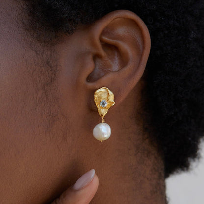 Detailed view of the Fleur d’Or gold and pearl drop earring worn on the ear, showing the sculptural petal and blue topaz accent.