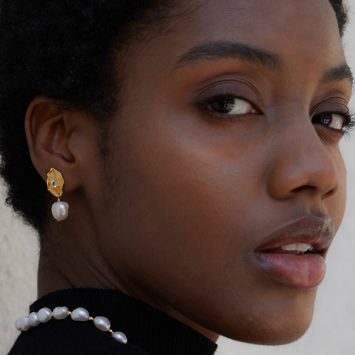 Model wearing Awakened Time Fleur d’Or gold drop earrings with pearl drops paired with a pearl necklace.
