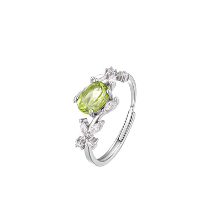 Close-up studio photograph of the Awakened Time Floral Ring. The ring features an oval-cut natural light green peridot gemstone set in 925 sterling silver, surrounded by a vine-and-leaf motif accented with sparkling cubic zirconia, shown on a white background.