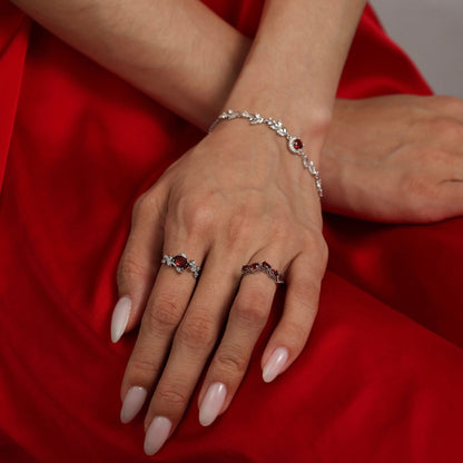 Lifestyle photograph of a woman wearing Awakened Time garnet jewelry against a red fabric background, featuring the floral-inspired garnet ring on her finger and a matching garnet-accented sterling silver bracelet on her wrist.