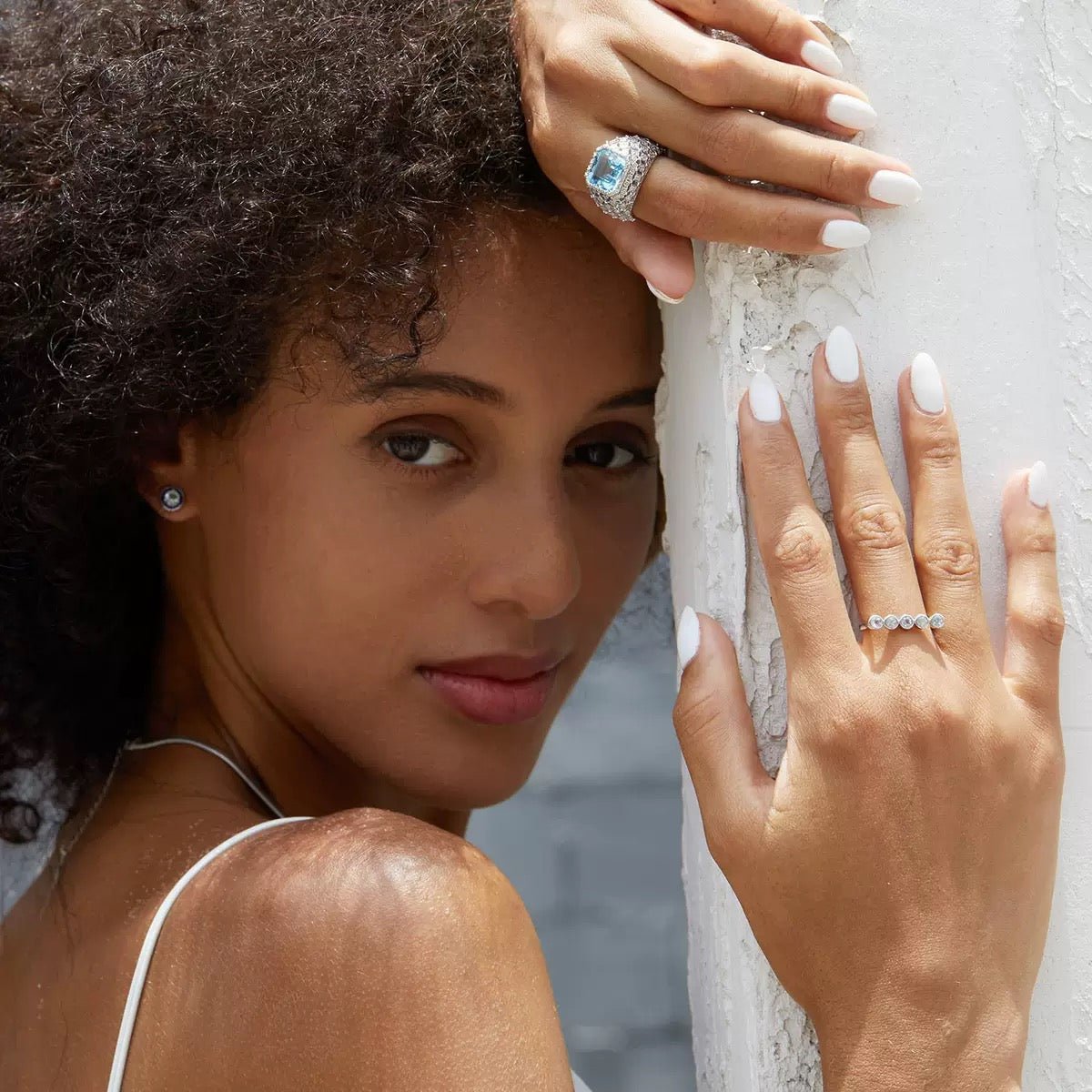 Awakened Time lifestyle shot of a model wearing a statement cocktail ring, a delicate diamond band, and matching earrings against a white pillar.