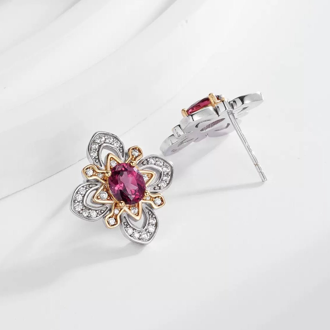 Pair of Awakened Time La Rosa di Firenze two-tone stud earrings displaying front and side post details with oval red garnets and pavé zirconia on a soft white background.
