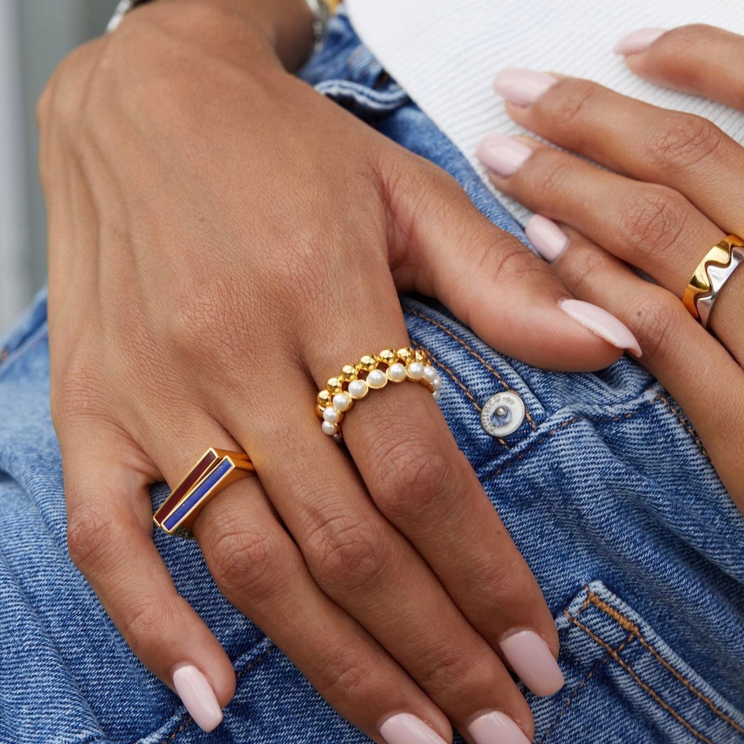 Close-up of a model's hands stacking The Lumière gold pearl ring with other jewelry by Awakened Time.