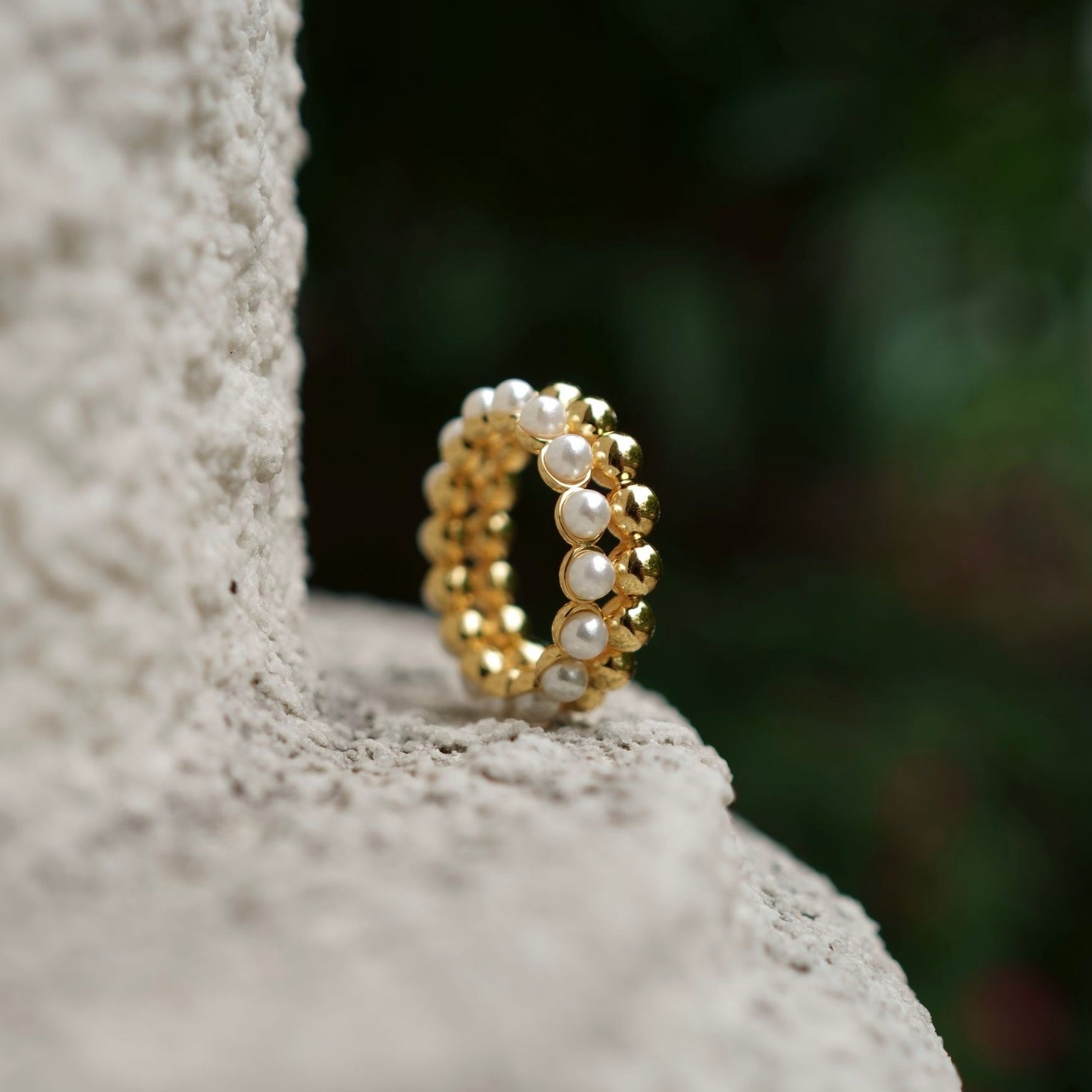The Lumière pearl ring displayed artfully on a stone surface, highlighting its delicate beaded texture by Awakened Time.