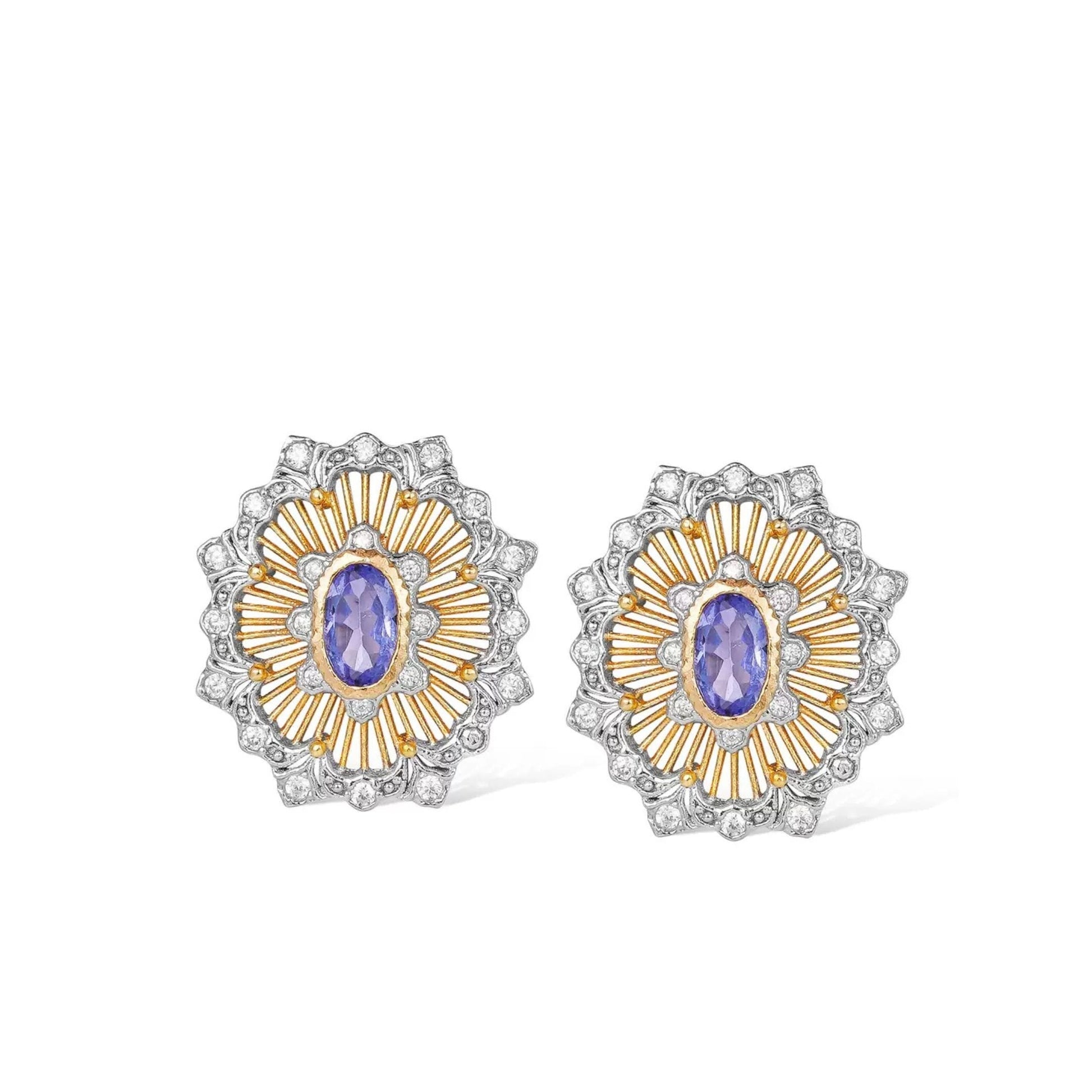 Pair of Awakened Time Medici’s Bloom two-tone stud earrings featuring oval natural tanzanite centers framed by gold sunburst rays and silver pavé zirconia scalloped borders on a white background.