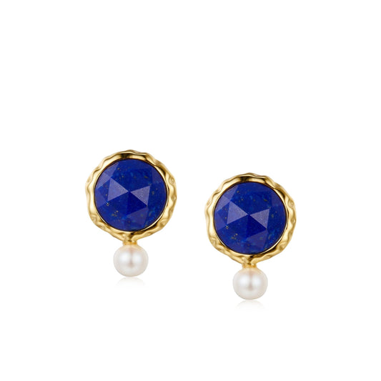 Pair of Awakened Time Ocean Pearl stud earrings featuring rose-cut faceted round lapis lazuli in wavy gold bezels with dangling petite white freshwater pearls on a white background.