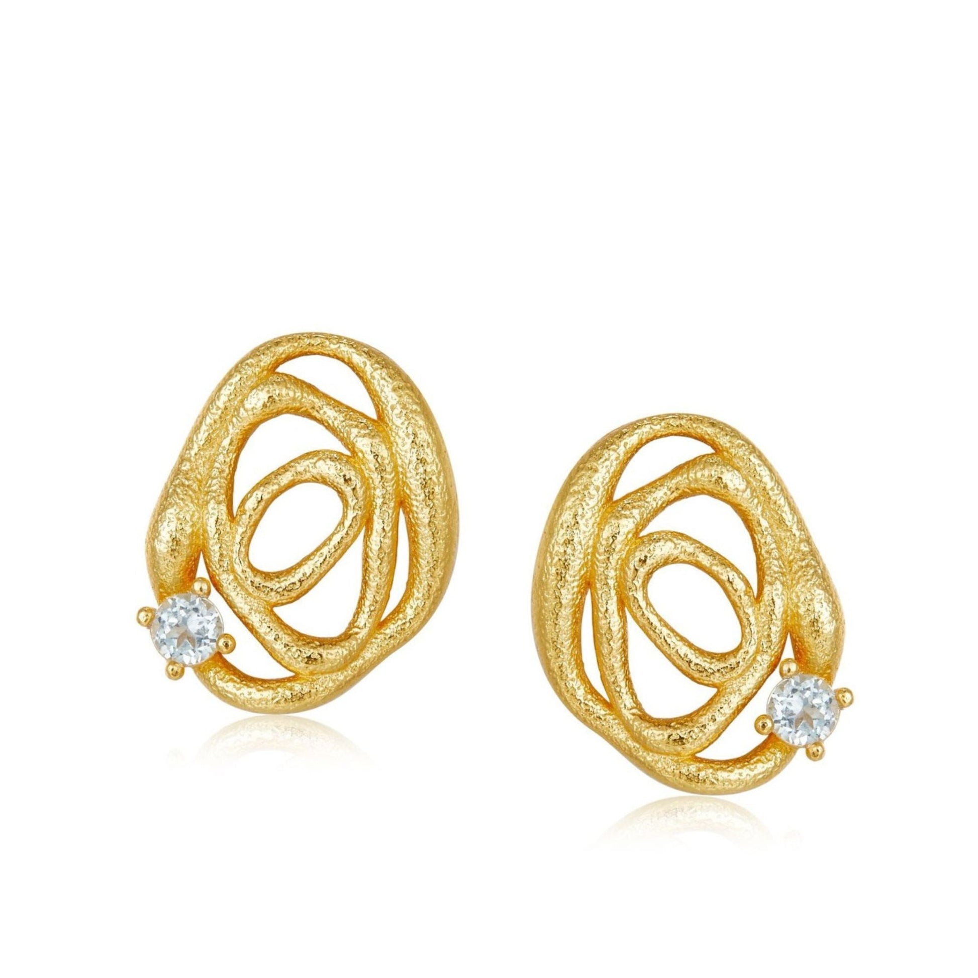 Pair of Awakened Time textured gold openwork wave stud earrings set with natural round blue topaz gemstones on a white background.