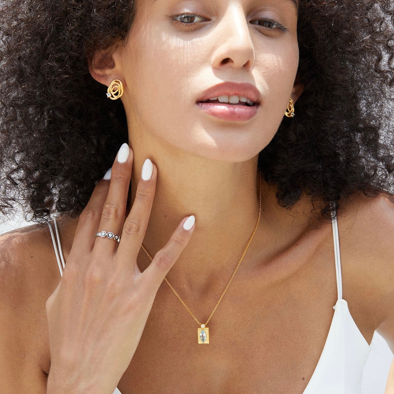 Close-up of a model posing with hand near her neck showcasing Awakened Time gold wave stud earrings and matching jewelry.