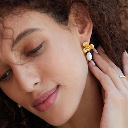 Model with hand near chin wearing Awakened Time gold brushed orchid earrings with baroque freshwater pearls.