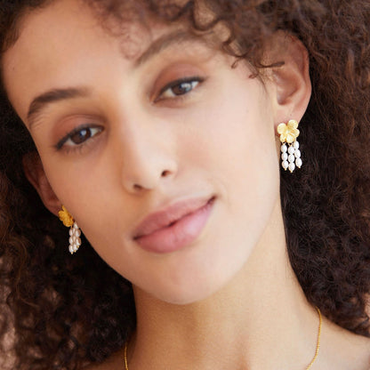 Frontal portrait of a model with curly hair wearing Awakened Time gold floral pearl cascade drop earrings.