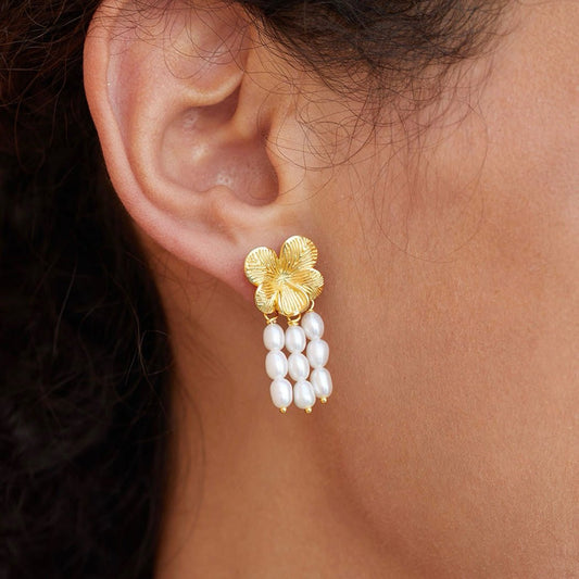 Close-up side view of a model wearing Awakened Time gold textured flower earrings with cascading pearl strands.
