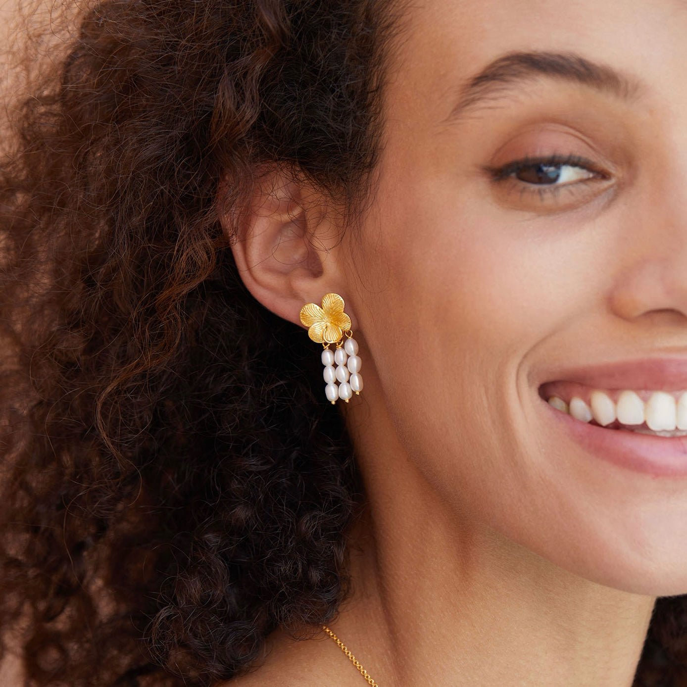 Model smiling while showcasing Awakened Time gold flower top and cascading freshwater pearl drop earrings.