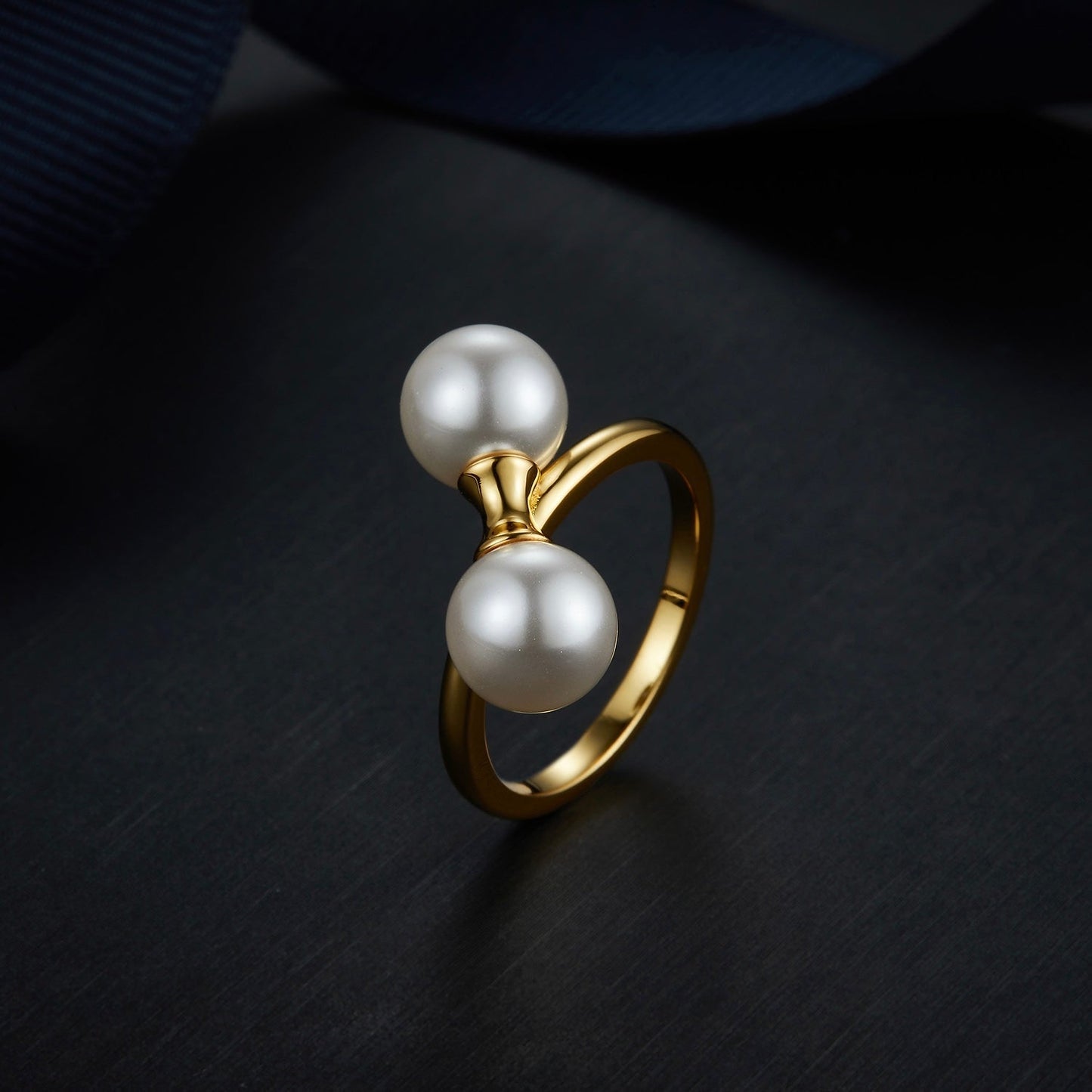 The Petite Symétrie pearl ring styled on a dark reflective background, highlighting its 18ct gold vermeil finish by Awakened Time.