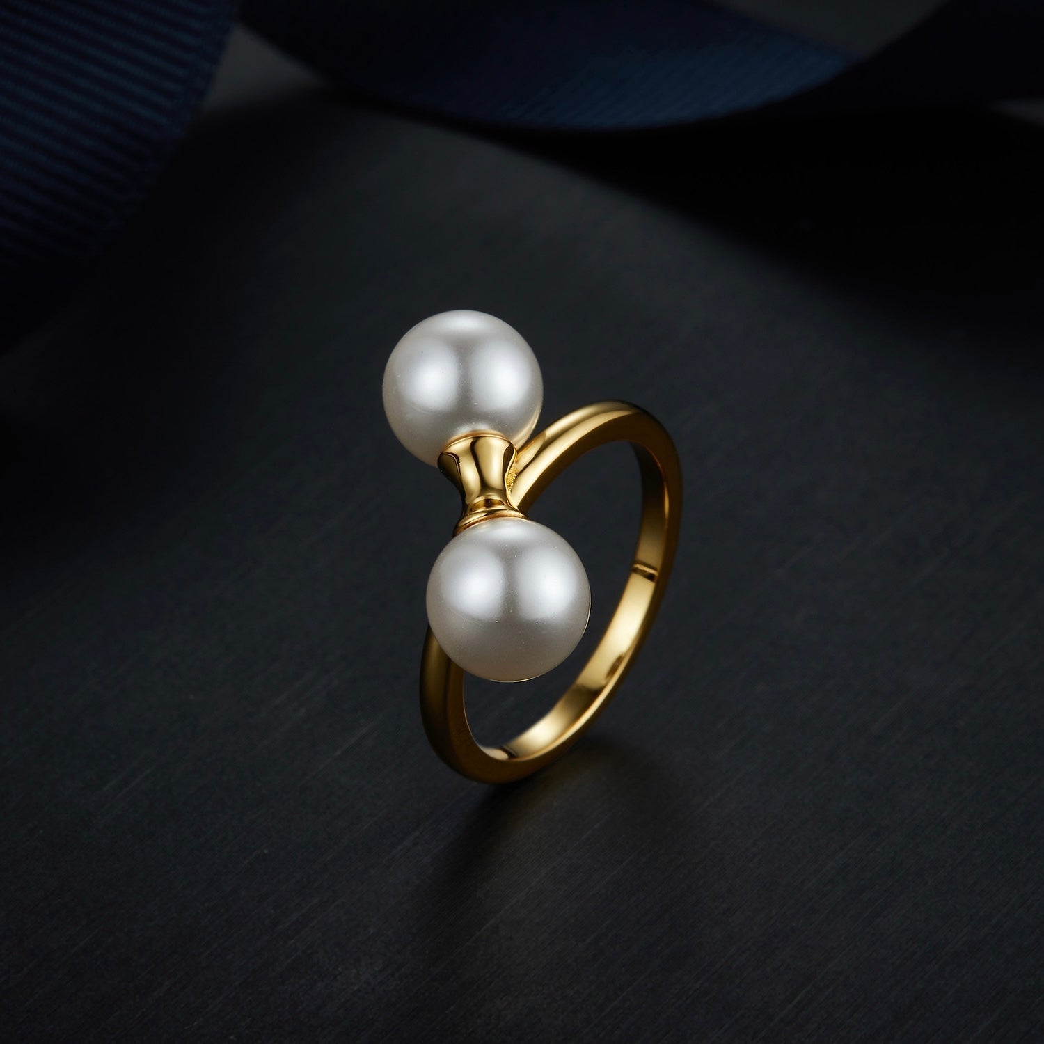 The Petite Symétrie pearl ring styled on a dark reflective background, highlighting its 18ct gold vermeil finish by Awakened Time.
