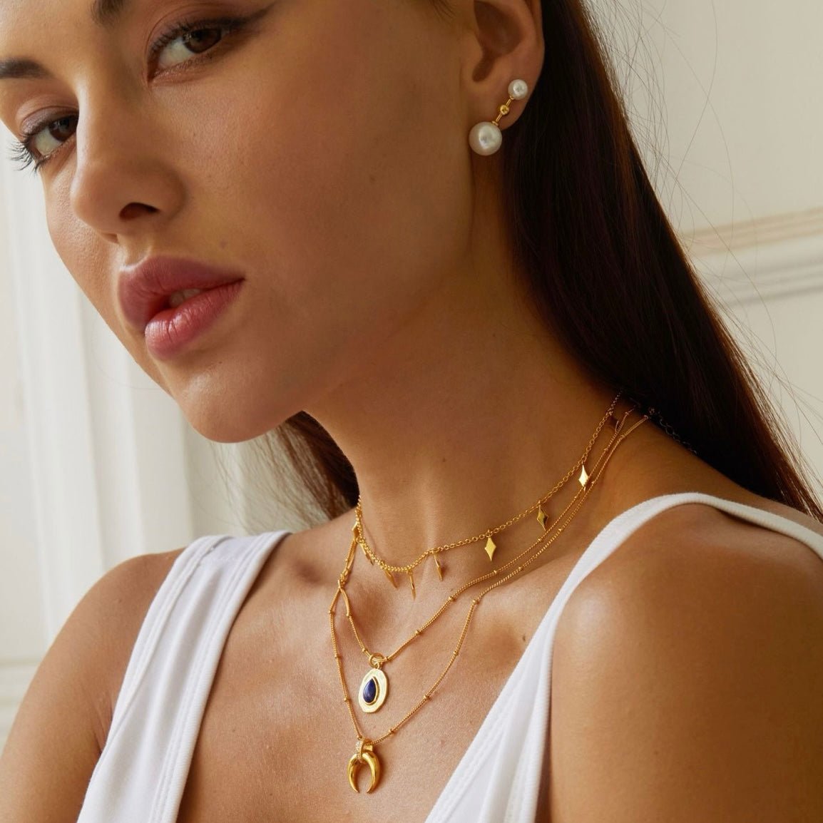 Model wearing the Awakened Time gold horn necklace with layered chains and pearl accents.