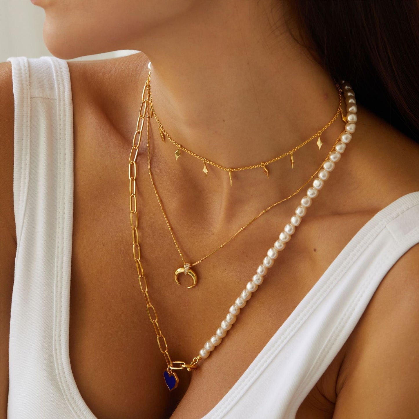 Awakened Time gold horn pendant necklace styled with fine chain and pearl necklaces over a white top.