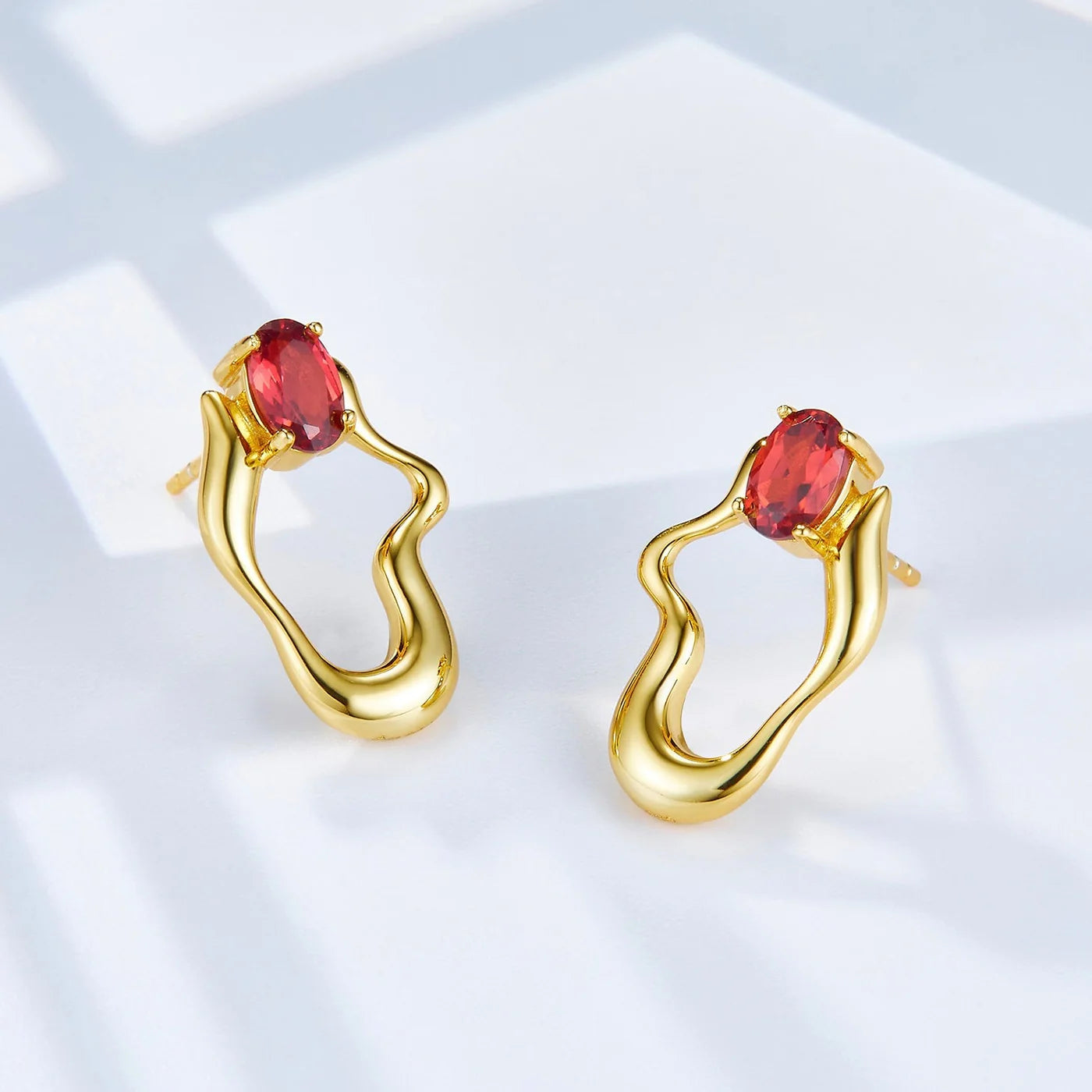 Awakened Time Rouge Wave gold earrings featuring red garnet gemstones and an elegant sculptural loop design.
