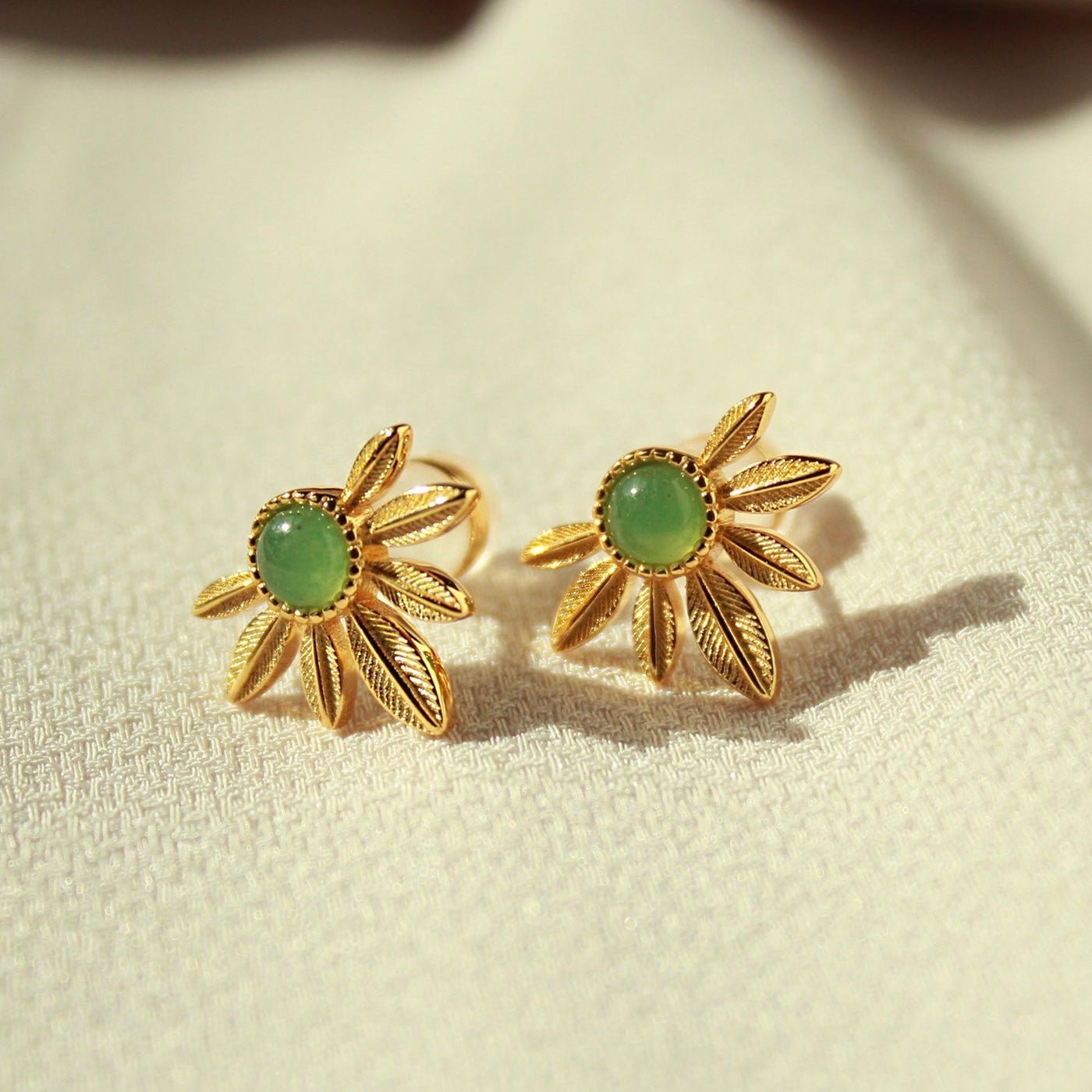 Close-up of Awakened Time green aventurine daisy earrings in 18ct gold vermeil resting on textured cream fabric.