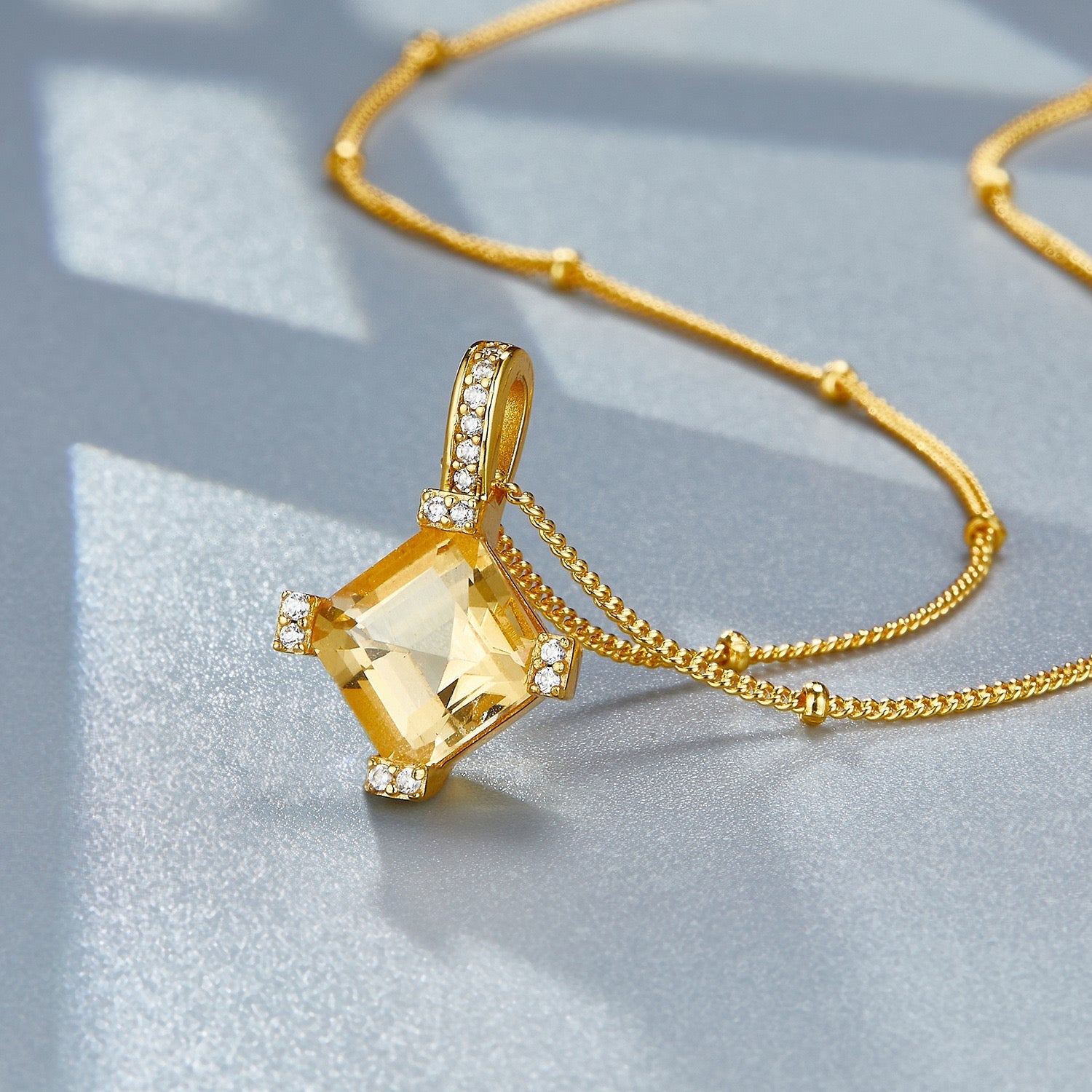 Studio detail view of the Awakened Time Stellar Frame citrine pendant catching the sunlight on a blue-grey surface.